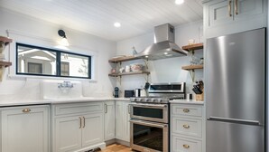 A modern kitchen with white cabinetry, stainless steel appliances, and a window above the sink. - Charming Loft Bedroom Cottage in Downtown White, 1 block away from everything (Whitefish)