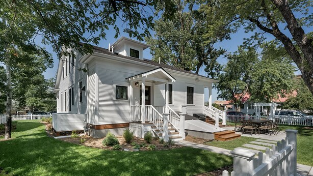A white two-story house with a front porch, a staircase, and a small front yard. - Charming Loft Bedroom Cottage in Downtown White, 1 block away from everything (Whitefish)