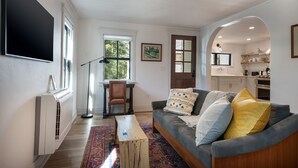 A living room with a sofa, a coffee table, a chair, a radiator, and a TV mounted on the wall. - Charming Loft Bedroom Cottage in Downtown White, 1 block away from everything (Whitefish)