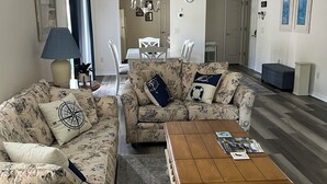 Una sala de estar con sofás de estampado floral, una mesa de centro de madera y una zona de comedor con una mesa y sillas blancas.