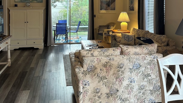 Una sala de estar con un sofá floral, un ventilador de techo y vistas al exterior a través de puertas de vidrio.