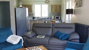 A living room with a sofa, two armchairs, a coffee table with chess pieces, and a kitchen in the background. - Maison à la Montagne Avec la vue sur le Montcalm Avec son Jardin Clôturé (Auzat)