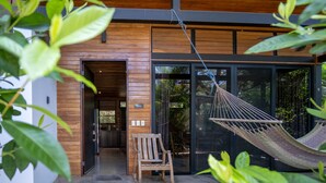 A modern building with a wooden exterior, a glass door entrance, a hammock, and a rocking chair outside.