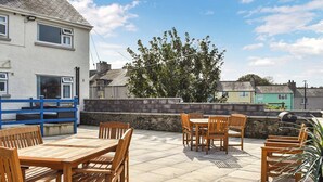 A patio with wooden furniture, a stone wall, and a view of houses in the background. - 4 bedroom accommodation in Amlwch (Amlwch)