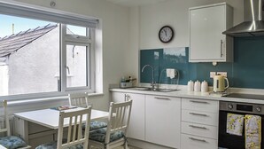 A compact kitchen with a window, white cabinets, a sink, and a clock on the wall. - 4 bedroom accommodation in Amlwch (Amlwch)