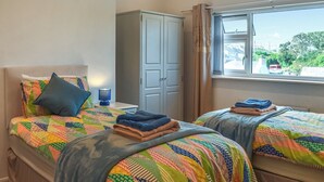 A bedroom with two beds, a wardrobe, and a window with a view of the outside. - 4 bedroom accommodation in Amlwch (Amlwch)