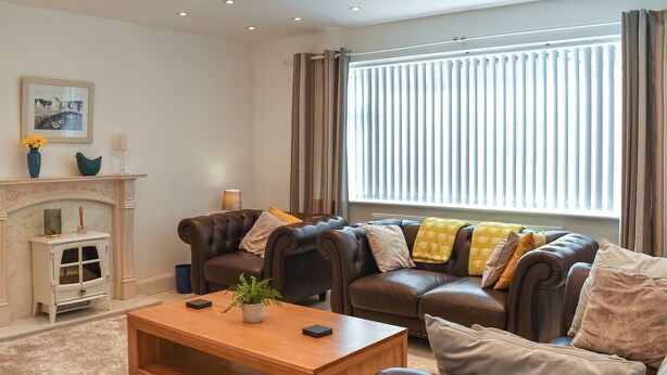 A modern living room with leather sofas, a wooden coffee table, and a fireplace. - 4 bedroom accommodation in Amlwch (Amlwch)