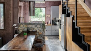 A modern kitchen with a stone island, wooden staircase, and a large pendant light. - Hidden Stone Chalet (Aigialeia)