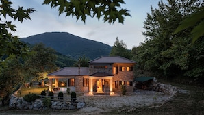 A two-story stone house with a tiled roof, a covered patio, and a view of a mountain. - Hidden Stone Chalet (Aigialeia)
