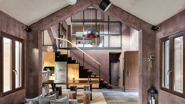 A spacious living area with a high ceiling, a staircase leading to an upper level, and a cozy seating area with a sofa and coffee table. - Hidden Stone Chalet (Aigialeia)