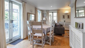 A dining area with a table and chairs, a sofa, a fireplace, and a large window with curtains. - 3 bedroom accommodation in Somerford Keynes (Somerford Keynes)