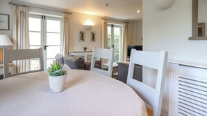 A dining area with a round table, chairs, a potted plant, and a television in the background. - 3 bedroom accommodation in Somerford Keynes (Somerford Keynes)