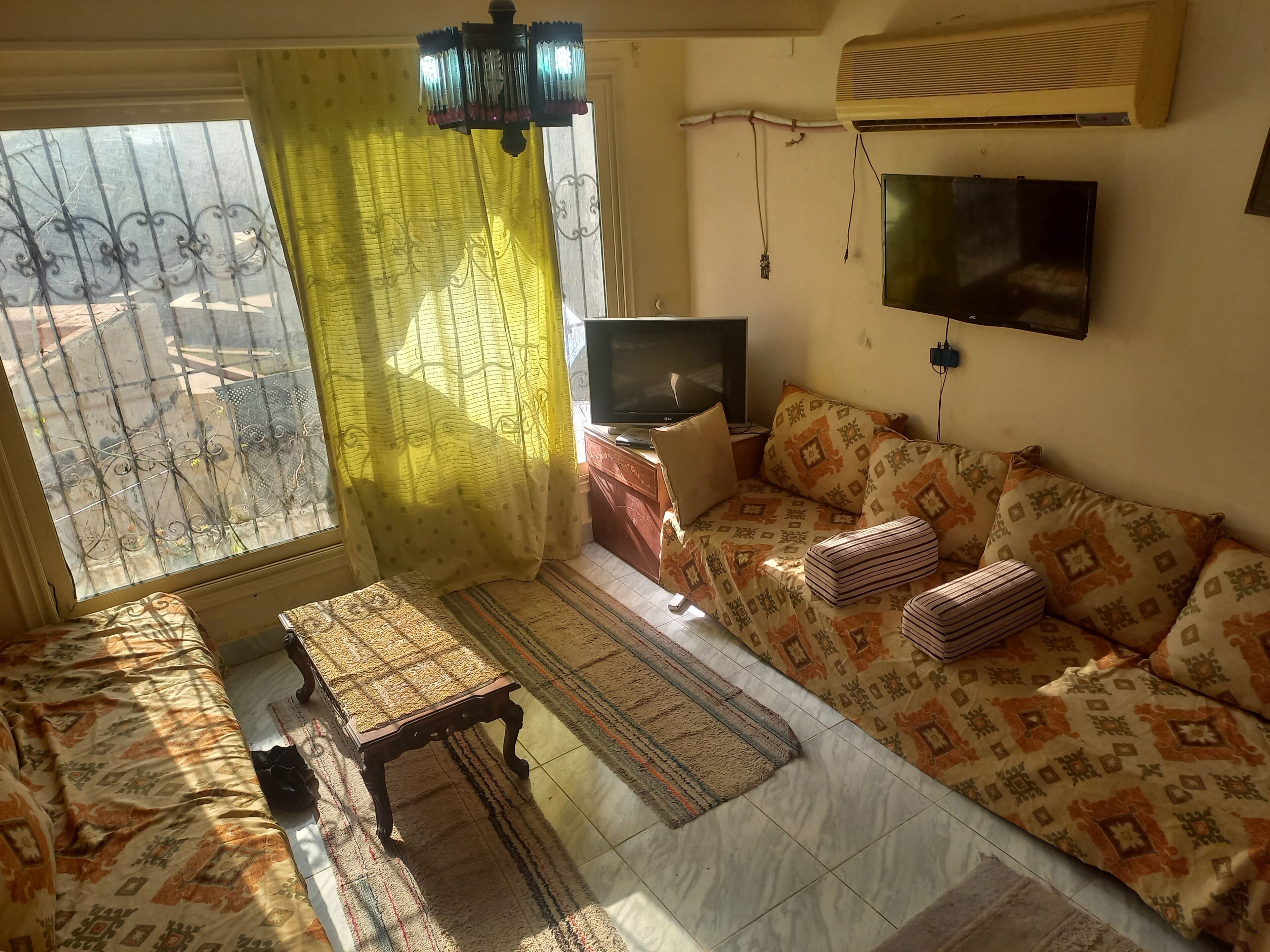 Uma sala de estar com sofá, televisão, mesa e tapete estampado.