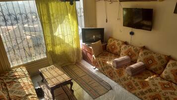 Uma sala de estar com sofá, televisão, mesa e tapete estampado.