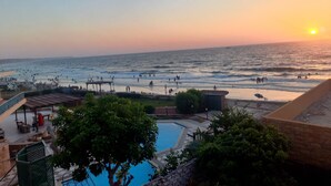 Zona de piscina con vista al océano y al atardecer.