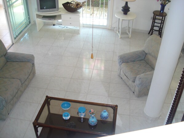 Un amplio salón con un conjunto de sofás, una mesa de centro con adornos, un televisor y un ventanal con vistas.