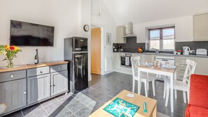 A modern kitchen with a black refrigerator, a dining table with chairs, and a television mounted on the wall. - 1 bedroom accommodation in Hewish (Hewish)