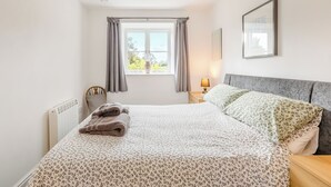 A bedroom with a bed, a window with curtains, a bedside lamp, a radiator, and a framed picture on the wall. - 1 bedroom accommodation in Hewish (Hewish)