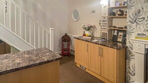 Een keuken met houten kastjes, een granieten aanrechtblad en een klein eiland. Er staat een rode kruk, een vaas met bloemen en een decoratief bord op de muur.