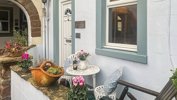 Een gezellig buiten zitgedeelte met een witte tafel en stoelen, omgeven door plantenbakken en een houten bank.