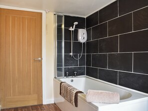 Un baño con puerta de madera, ducha con cabezal de mano, bañera y paredes de azulejos negros.