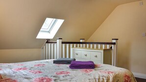 Een slaapkamer met een schuine plafond, een dakraam, een bed met bloemenbeddengoed, een nachtkastje en een dressoir met laden.
