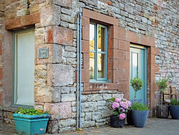 A stone building with a sign reading 'Bar n End,' a window with shutters, and potted plants outside.