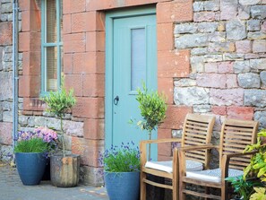 A rustic building with a green door, stone walls, and wooden chairs outside.