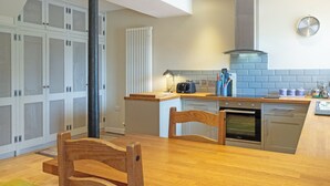 Eine moderne Küche mit Holztisch, eingebauten Schränken, Dunstabzugshaube und einer Wanduhr.