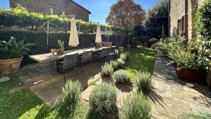 Eine Terrasse mit Steintisch und -stühlen, umgeben von Kübelpflanzen und einer Steinmauer.