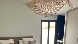 Un dormitorio con una cama grande, suelo de madera, ventilador de techo y vistas al exterior a través de una puerta corredera.