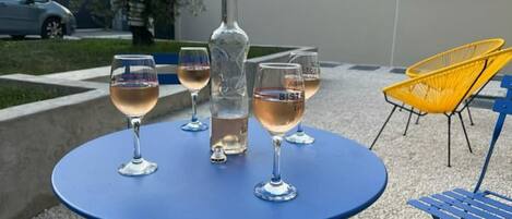Una mesa azul al aire libre con cuatro copas de vino y una botella, rodeada de sillas y un edificio al fondo.