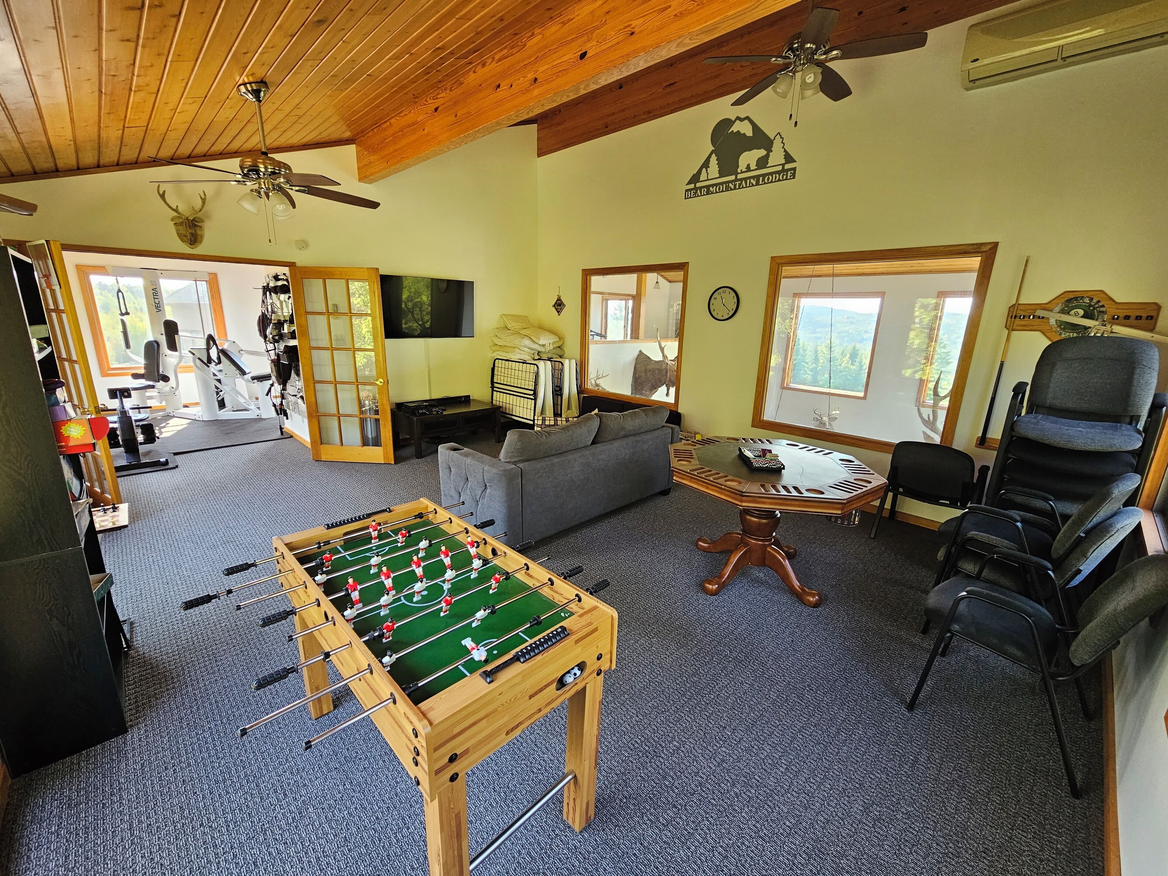 A cozy living room with a foosball table, a sofa, a dining table, and a large window offering a view of the outdoors.