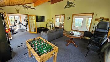 A cozy living room with a foosball table, a sofa, a dining table, and a large window offering a view of the outdoors.