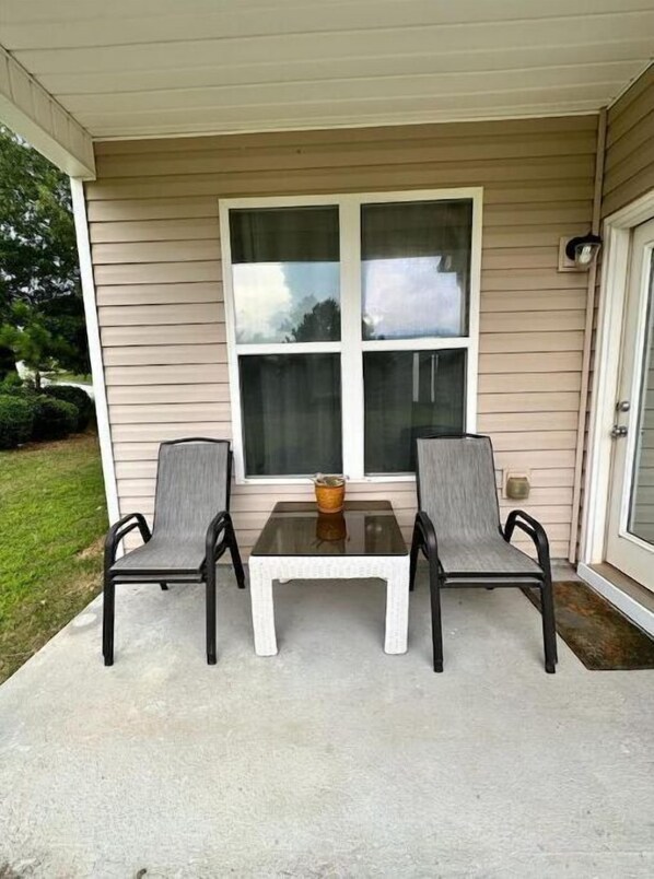 A covered patio with a table and two chairs, a window, and a door. - Sleeps 8: King sized bed - Home away from home, yet close to everything! (Douglasville)