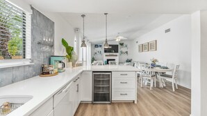 A modern kitchen with white cabinetry, a built-in dishwasher, and a dining area with white chairs and a table. - Beach & City Oasis: Moments from Siesta Key Beach (Sarasota)