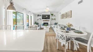 A spacious living area with a white dining table, white chairs, and a sofa. There is a TV mounted on the wall, a ceiling fan, and a fireplace. - Beach & City Oasis: Moments from Siesta Key Beach (Sarasota)