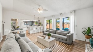 A spacious living room with a grey sofa, a coffee table, and a dining area with white chairs and a table. - Beach & City Oasis: Moments from Siesta Key Beach (Sarasota)