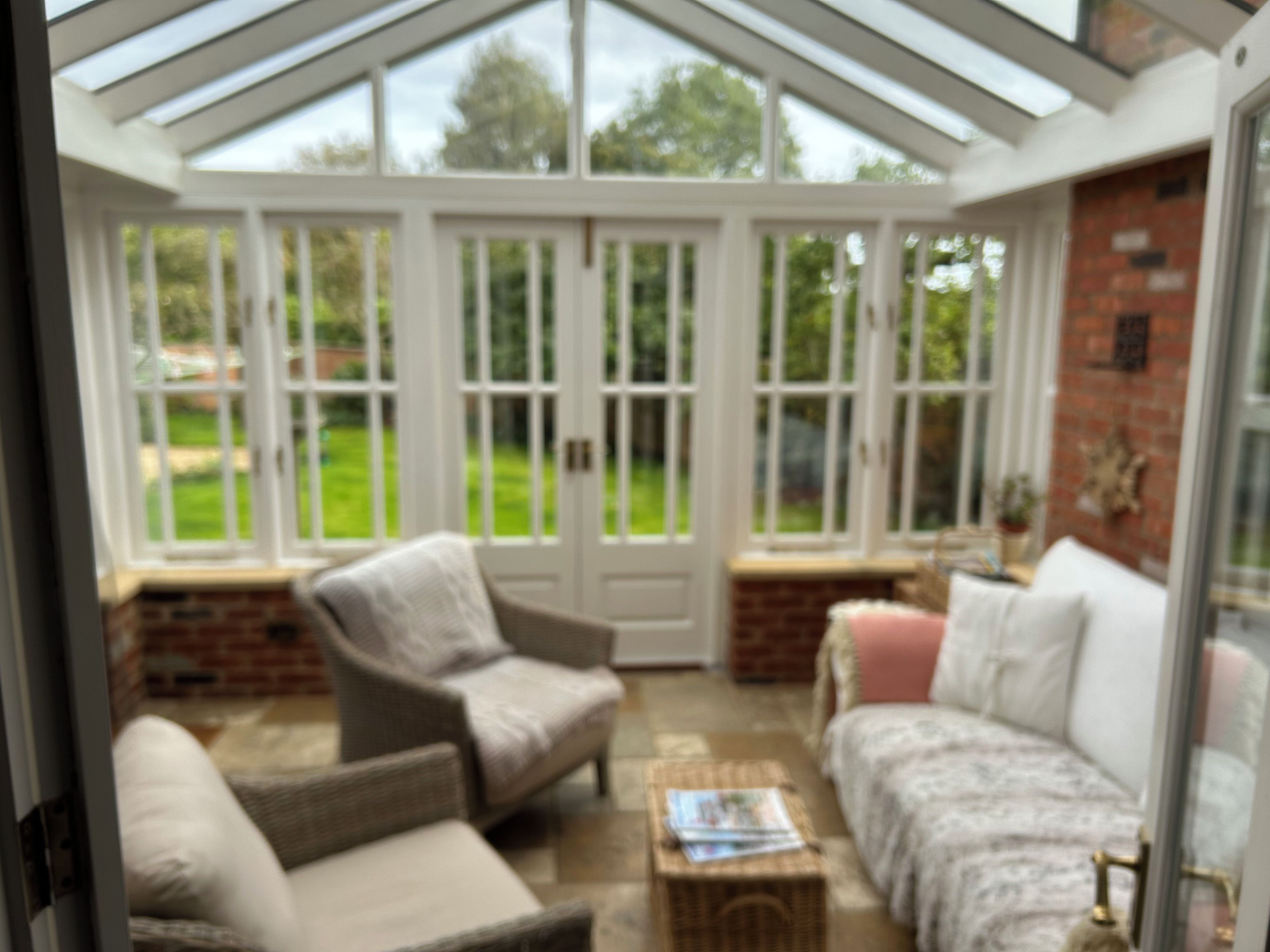 A conservatory with a glass roof, wicker furniture, and a brick wall.