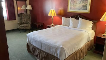 Una habitación de hotel con una cama grande, una silla, una mesita, una lámpara y un cuadro en la pared.
