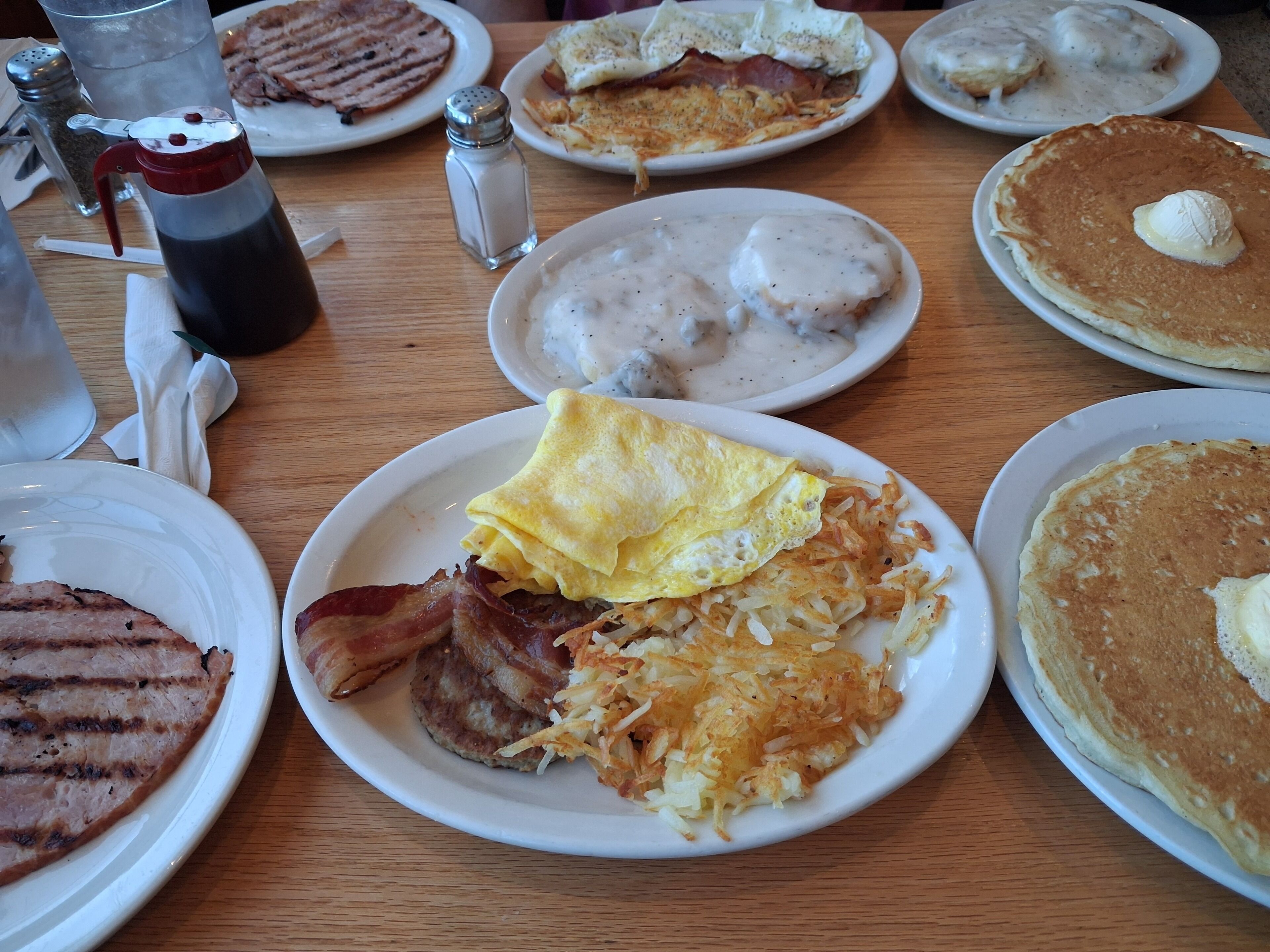A breakfast table with plates of food including eggs, bacon, hash browns, pancakes, and waffles.