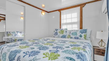 A bedroom with a large bed, a nightstand, a mirror, and a window with blinds.