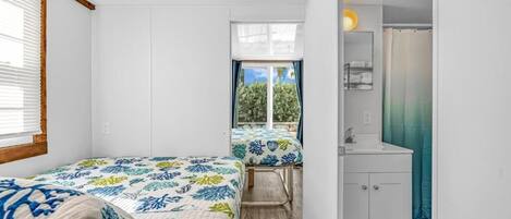 A compact bedroom with two beds, a small bathroom, and a view of the outdoors.