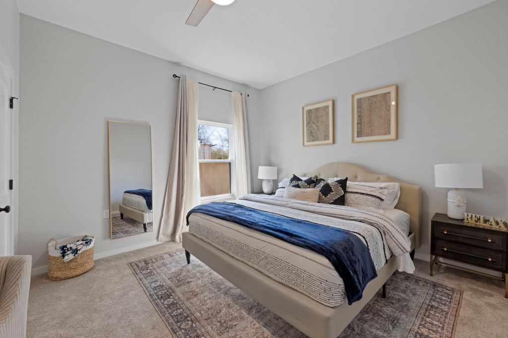 A bedroom with a bed, bedside tables, a mirror, and a window with curtains.