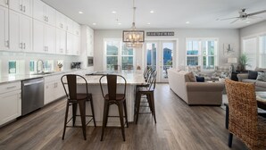 A modern kitchen with white cabinets, a central island with stools, and a dining area with a sofa and chairs. - Awesome Beach House, Private Pool, Gulf View (Navarre)