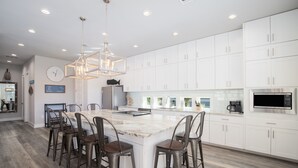 A modern kitchen with white cabinets, a large island with bar stools, and a hanging light fixture. - Awesome Beach House, Private Pool, Gulf View (Navarre)