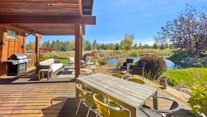 Eine Holzterrasse mit Grill, Gartenmöbeln und Blick auf einen See.
