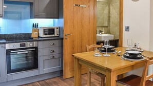 A kitchen with grey cabinets, a microwave, an oven, and a dining table set with plates and glasses. - Intimate and inviting, this couples retreat is a cosy haven for two. (South Kilvington, near Thirsk)
