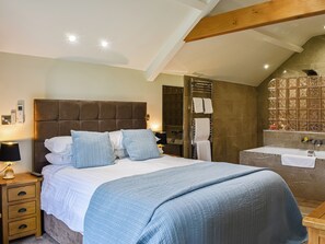 Un dormitorio con una cama grande, mesitas de noche, un tocador, un calentador de pared, un perchero y un baño con bañera y espejo.