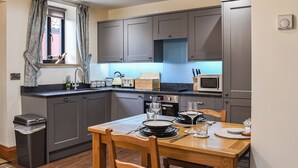 A modern kitchen with grey cabinets, a wooden dining table set with plates, glasses, and cutlery, and a window with curtains. - Intimate and inviting, this couples retreat is a cosy haven for two. (South Kilvington, near Thirsk)
